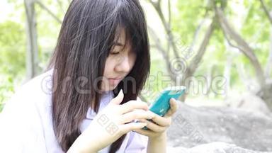泰国学生十几岁的漂亮女孩用她的智能手机坐在公园里。
